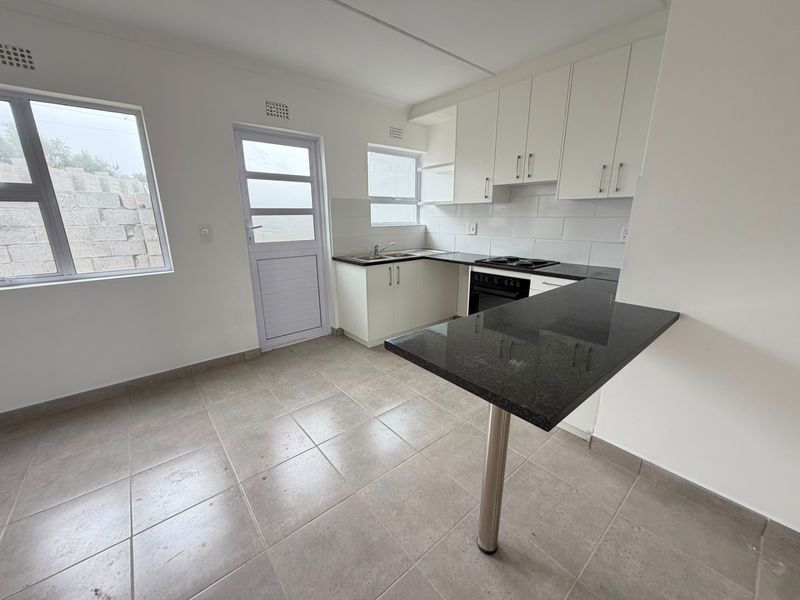 A clean, functional kitchen featuring white cabinetry, dark granite countertops, a breakfast bar, and tiled flooring with direct access to the exterior.