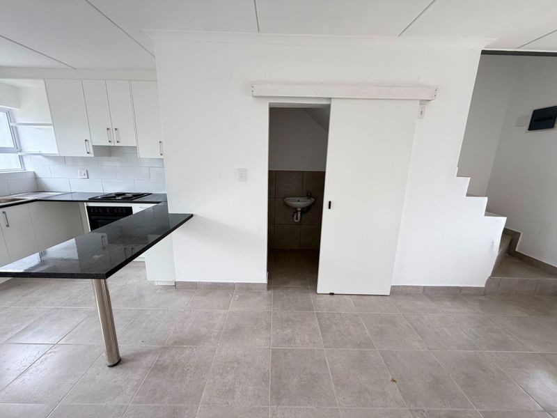 Open plan kitchen area featuring granite countertops, built-in cabinetry, and a sliding door leading to a small utility space with a basin.