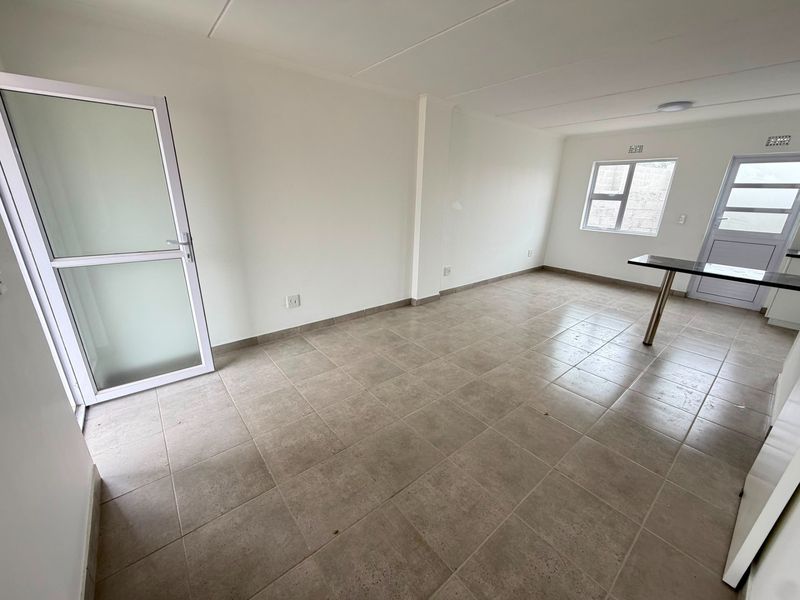 An open-plan living area featuring neutral tiled flooring, aluminium-framed doors and windows, and a built-in breakfast bar counter.