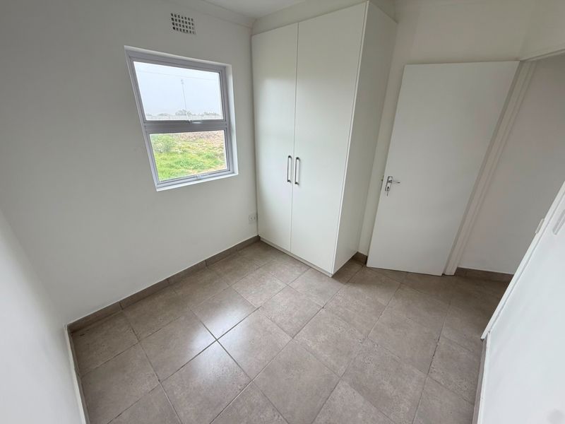 A clean, empty bedroom featuring neutral tiled flooring, a built-in wardrobe, and a window providing natural light.