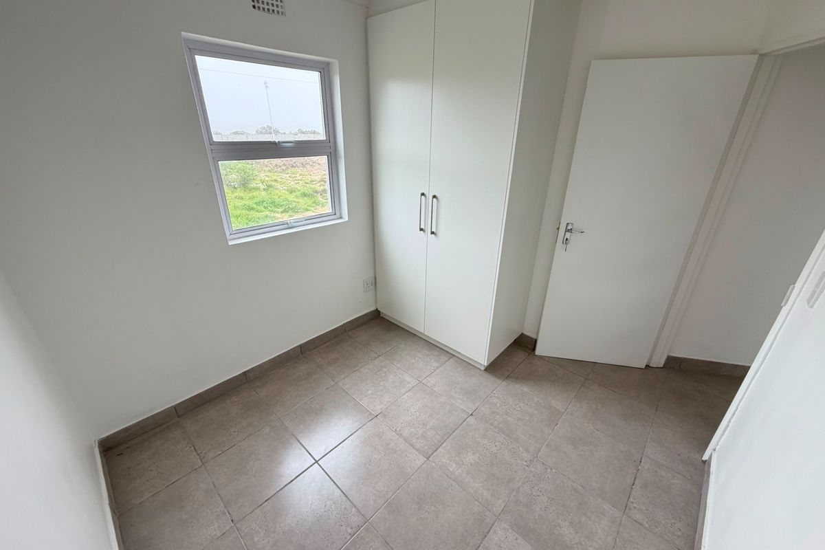 A clean, empty bedroom featuring neutral tiled flooring, a built-in wardrobe, and a window providing natural light.