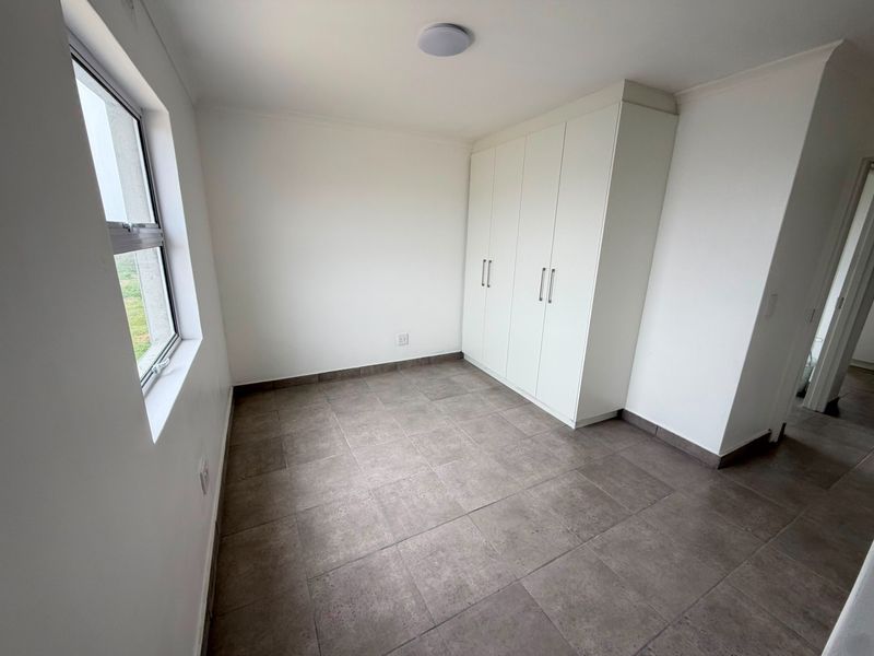 A clean, empty bedroom featuring neutral tiled flooring and white built-in cupboards, offering a versatile space ready for personalization.