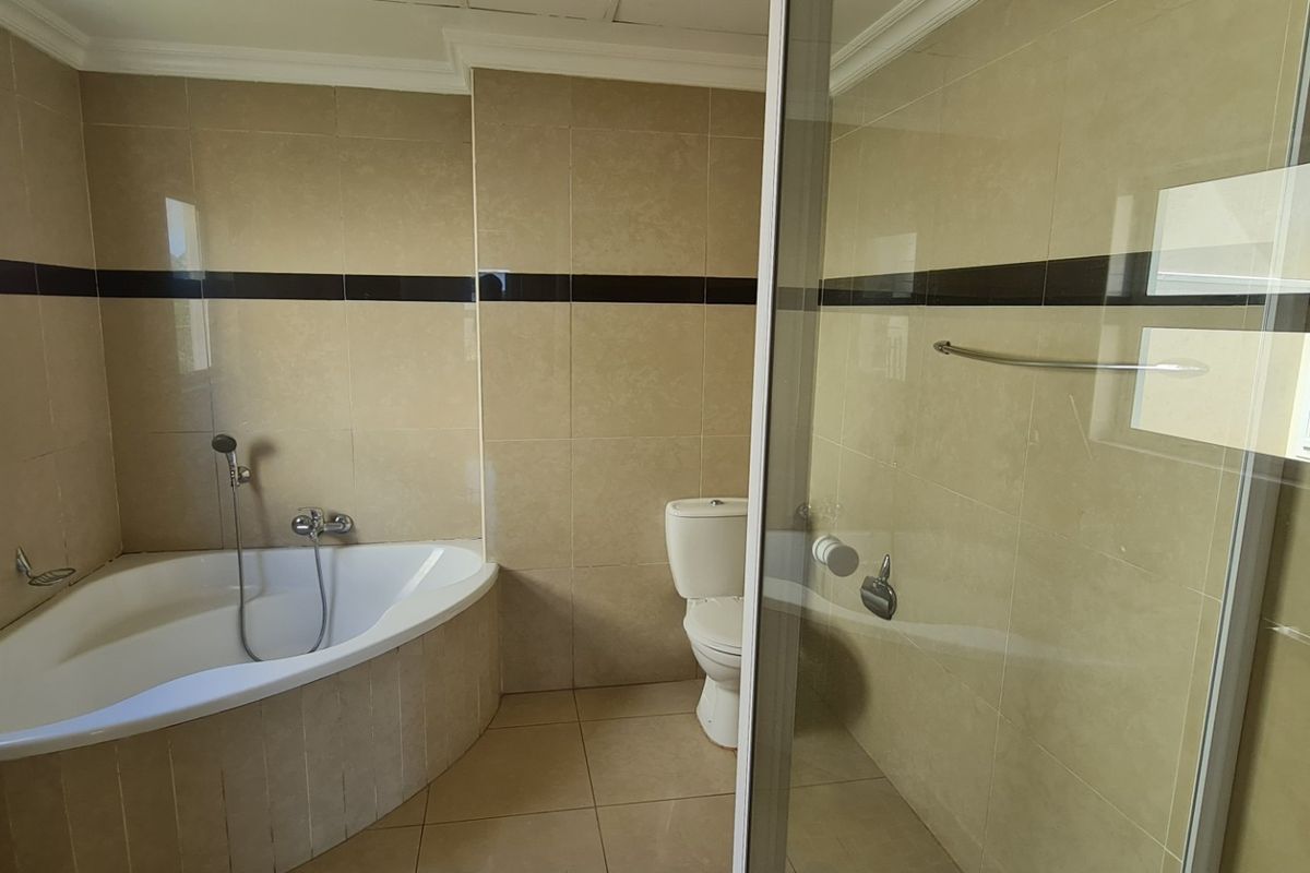 A spacious bathroom featuring a corner bathtub, a separate shower enclosure with a glass door, and a toilet, finished with neutral wall and floor tiles.