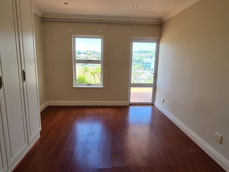 A bright, empty bedroom featuring laminate flooring, built-in cupboards, and direct access to a balcony through a glass door.