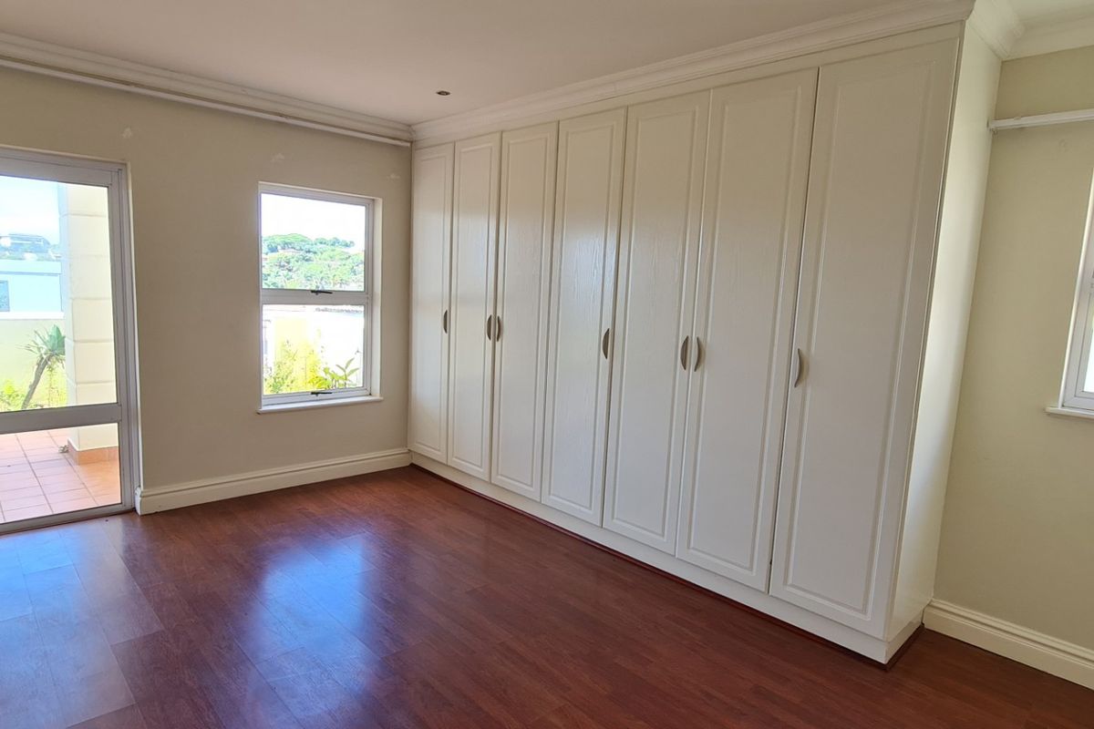 A bright, empty bedroom featuring laminate flooring, extensive built-in cupboards, and direct access to an outdoor balcony area.