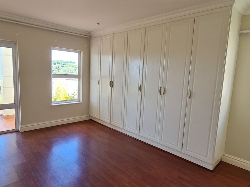 A bright, empty bedroom featuring laminate flooring, extensive built-in cupboards, and direct access to an outdoor balcony area.