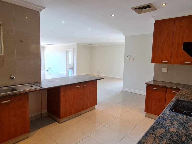 Spacious open-plan kitchen featuring granite countertops, cherry wood cabinetry, and integrated appliances, flowing seamlessly into the adjacent living area.