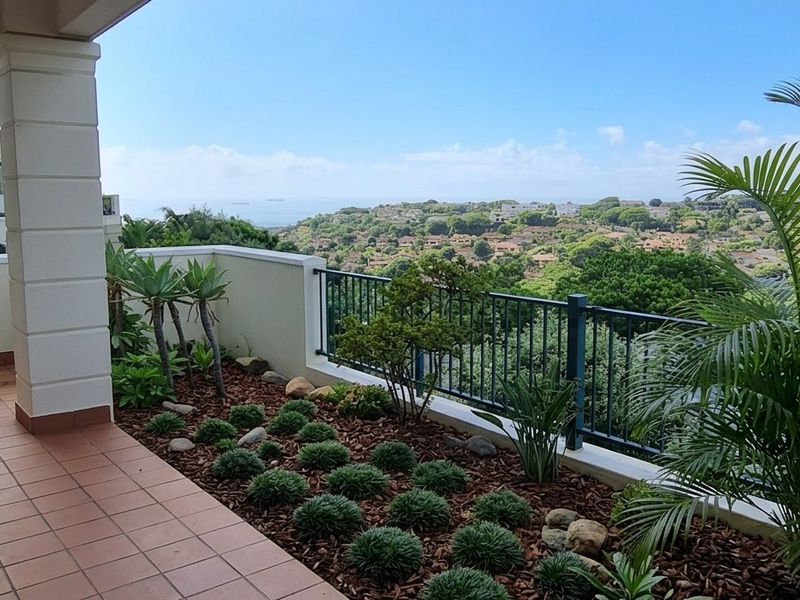 A spacious covered balcony featuring tiled flooring, a secure metal balustrade, and expansive elevated views of the surrounding landscape.