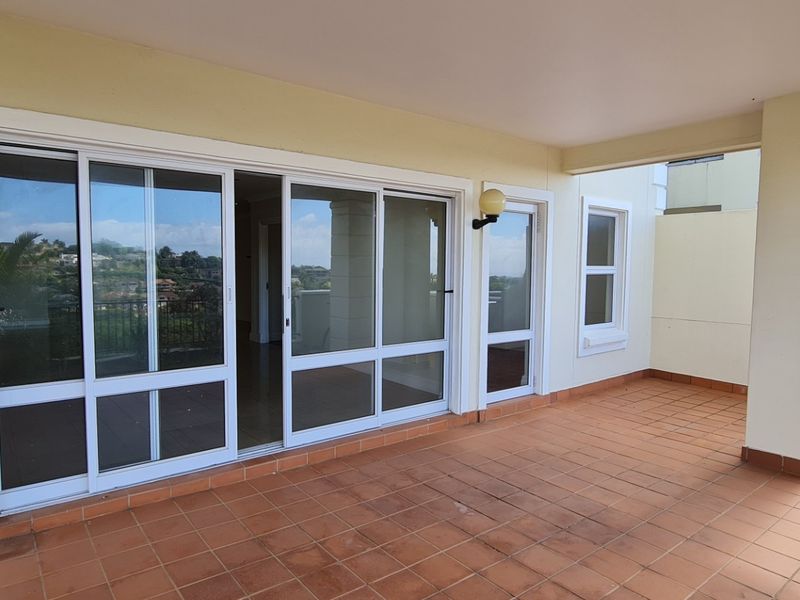 A spacious covered balcony featuring terracotta tiling and large sliding glass doors, offering a seamless transition to the interior living space.