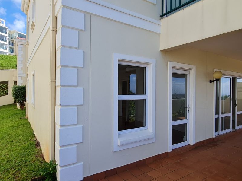 A well-maintained rear exterior view of the apartment featuring a tiled patio, sliding glass doors, and decorative quoins on the building facade.