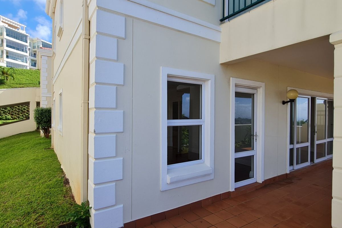 A well-maintained rear exterior view of the apartment featuring a tiled patio, sliding glass doors, and decorative quoins on the building facade.