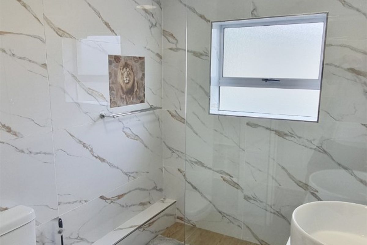 Modern bathroom featuring marble-look wall tiles, a frameless glass shower enclosure, a floating vanity with a vessel sink, and wood-look flooring.