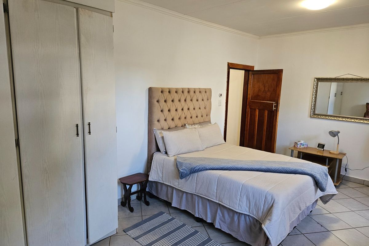 A bedroom featuring tiled flooring, built-in cupboards, and a wooden door, providing a functional and neutral living space.