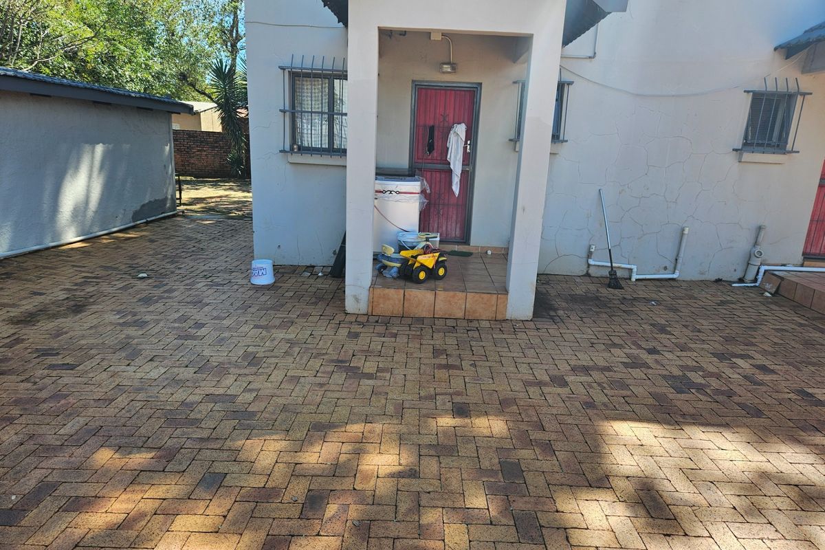 Rear exterior view of the property featuring a paved courtyard, covered entrance porch, and security bars on windows.