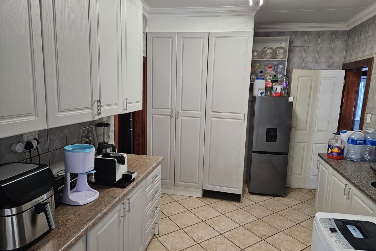 Functional kitchen featuring ample built-in cabinetry, laminate countertops, tiled backsplash, and durable floor tiles with a dedicated pantry storage area.