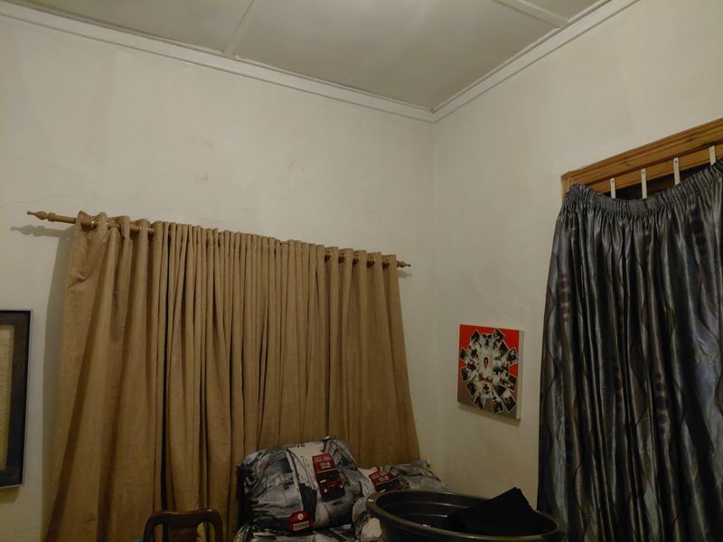 A bedroom interior featuring plain walls, ceiling cornicing, and window treatments.