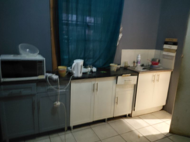 A small kitchen area featuring a mix of white and grey cabinetry, a stainless steel sink, and tiled flooring.
