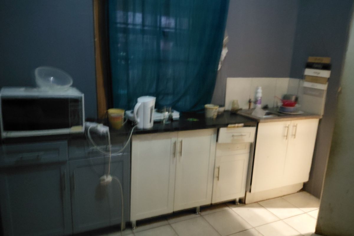 A small kitchen area featuring a mix of white and grey cabinetry, a stainless steel sink, and tiled flooring.