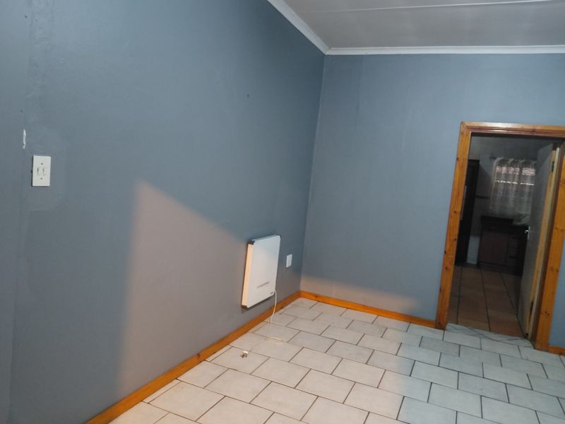 A simple, empty room featuring tiled flooring, blue-painted walls, and a wall-mounted electric heater, with a doorway leading to an adjacent space.