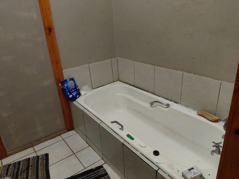 A functional bathroom featuring a built-in bathtub with tiled surround and chrome fixtures, requiring cosmetic updates to the wall finishes and trim.