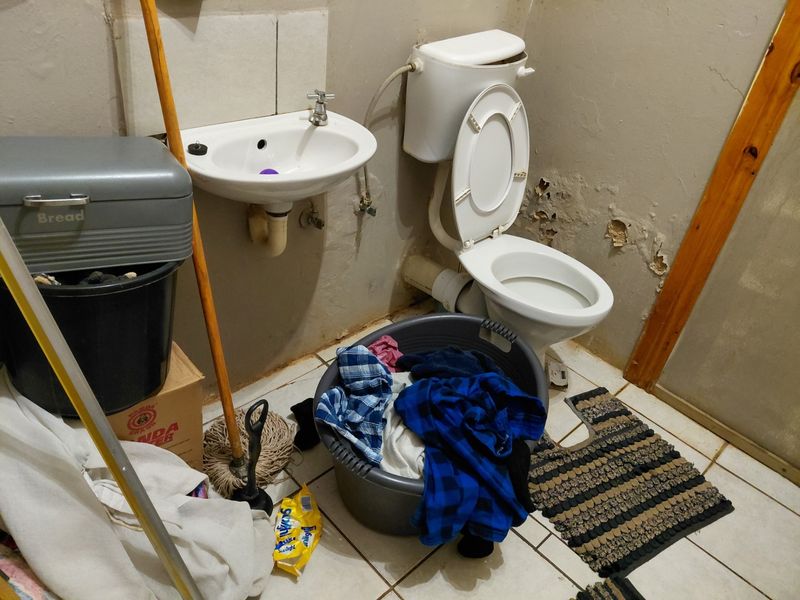A small bathroom featuring a wall-mounted basin and toilet, currently requiring significant maintenance and cosmetic repairs to the wall finishes.