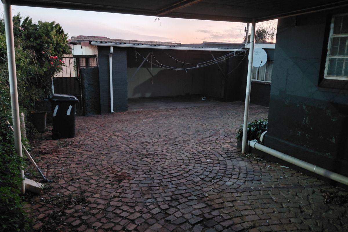 A paved outdoor courtyard area featuring a covered carport structure and brick exterior walls, providing a functional space for parking or outdoor use.