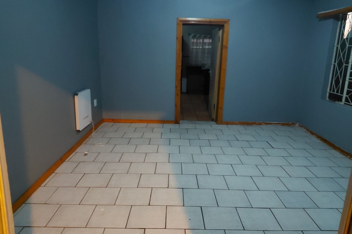 An empty living room featuring tiled flooring, blue painted walls, and a wall-mounted heater, providing a blank canvas for interior design.