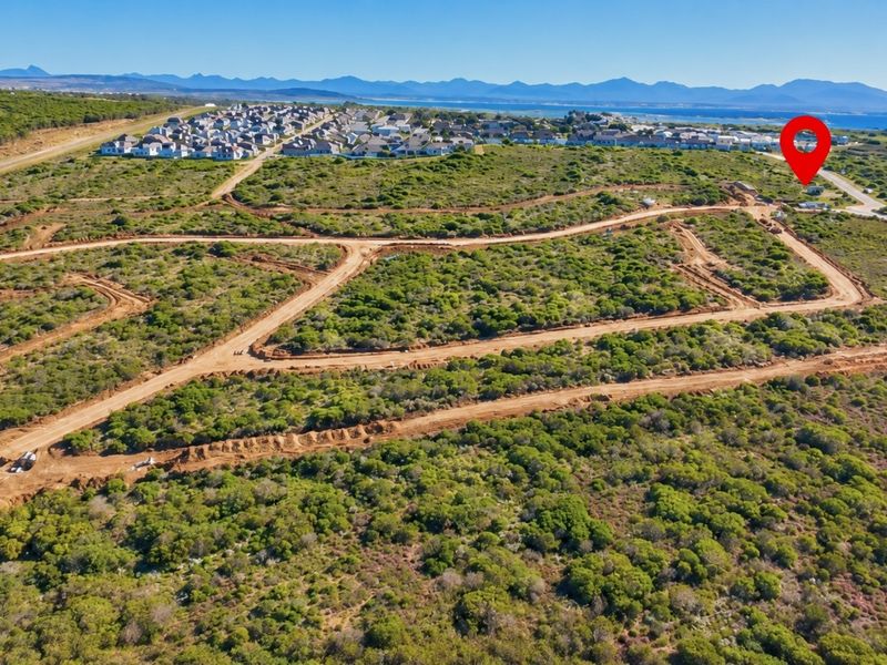 Aerial view of a residential development site featuring cleared plots, unpaved access roads, and surrounding coastal landscape.