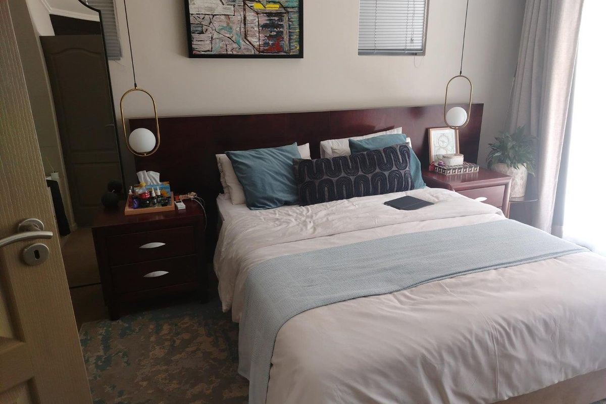 A well-maintained bedroom featuring a built-in dark wood headboard, modern pendant lighting, and dual windows with blinds.