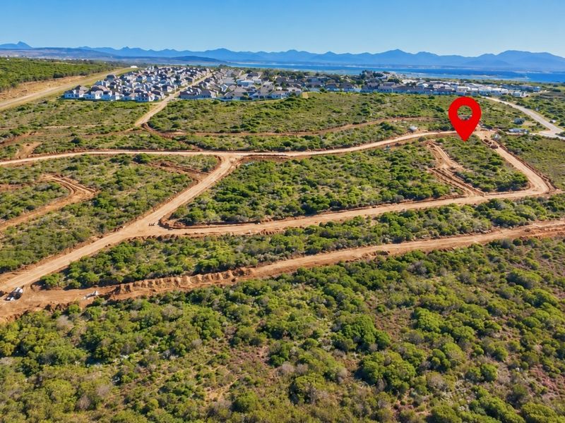Aerial view of a vacant residential land plot within a developing estate, featuring natural coastal vegetation and established dirt access roads.