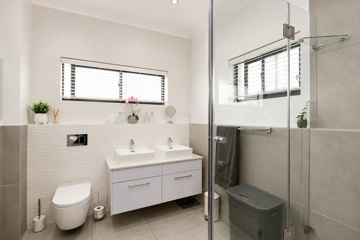 Modern bathroom featuring a double vanity with vessel sinks, wall-mounted toilet, and a glass-enclosed shower with contemporary tiling.