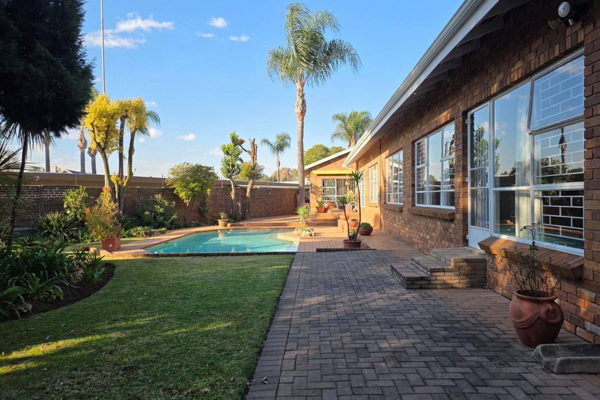 A well-maintained rear garden featuring a swimming pool, paved patio area, and established landscaping adjacent to the brick-built house exterior.