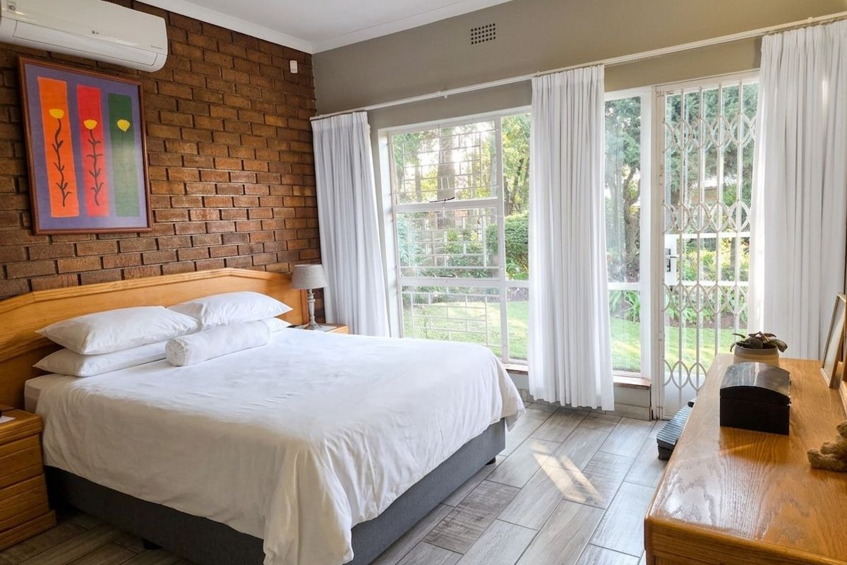A bright bedroom featuring a rustic exposed brick feature wall, tiled flooring, and large windows with direct access to the garden.