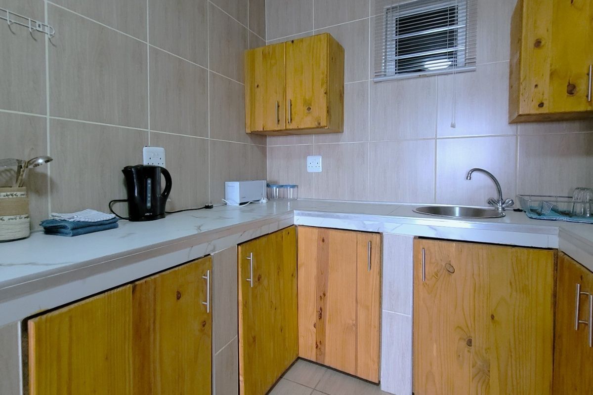 A functional kitchen area featuring wooden cabinetry, a stainless steel sink, and tiled splashbacks, providing a practical workspace for daily food preparation.