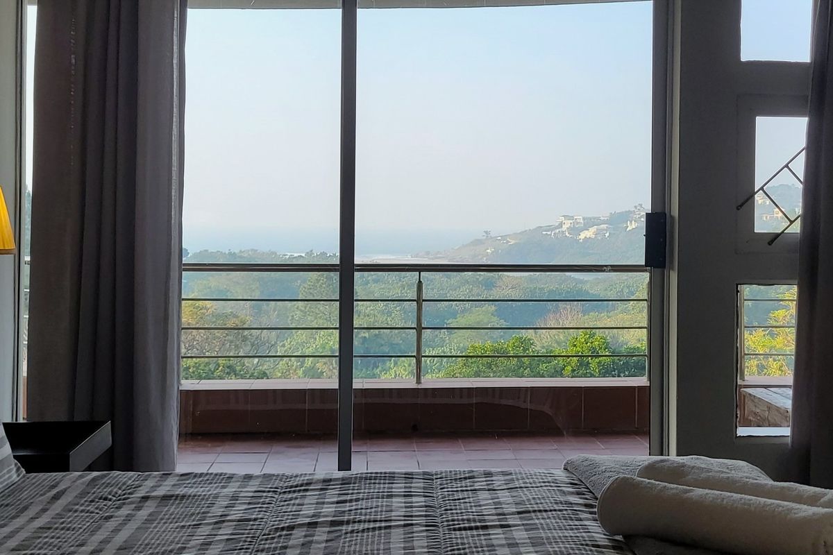 A bedroom featuring a large sliding glass door that opens onto a balcony with scenic coastal and landscape views.