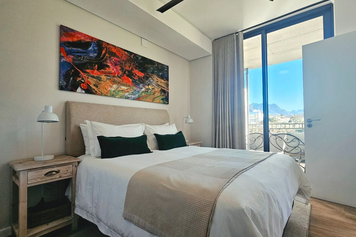 A well-maintained bedroom featuring laminate flooring, a ceiling fan, and a sliding glass door providing access to a balcony with mountain views.