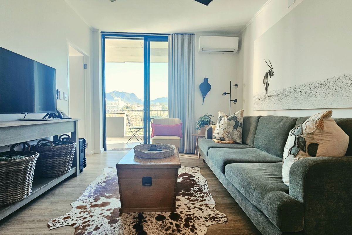 A well-maintained living room featuring laminate flooring, a wall-mounted air conditioning unit, and direct access to a private balcony with mountain views.