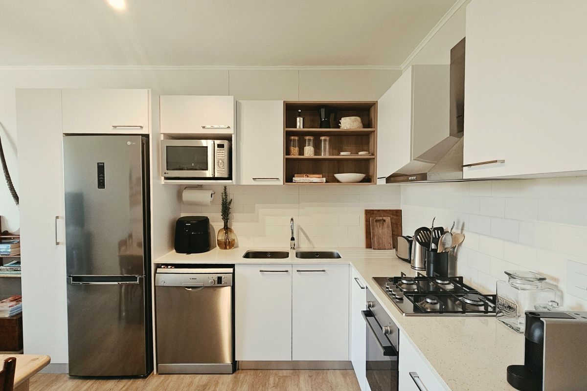 Modern kitchen featuring white cabinetry, subway tile backsplash, stainless steel appliances including a gas hob, oven, extractor fan, and integrated dishwasher.