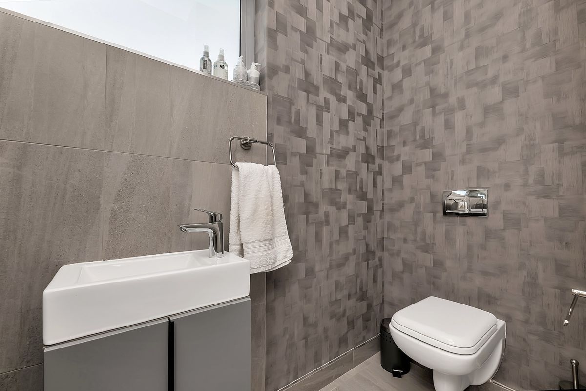 Modern guest bathroom featuring a wall-mounted toilet, sleek vanity basin, and contemporary textured wall tiling.