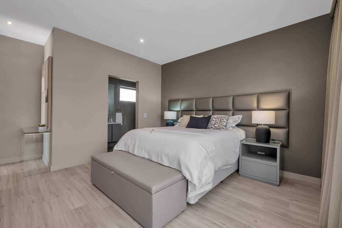 A well-maintained bedroom featuring modern light wood-look flooring, a neutral color palette, and an integrated upholstered headboard, with an adjoining en-suite bathroom.
