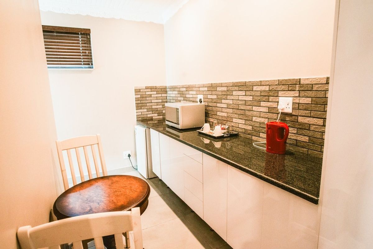 A compact kitchenette area featuring modern white cabinetry, granite countertops, and a decorative brick-style tiled backsplash.
