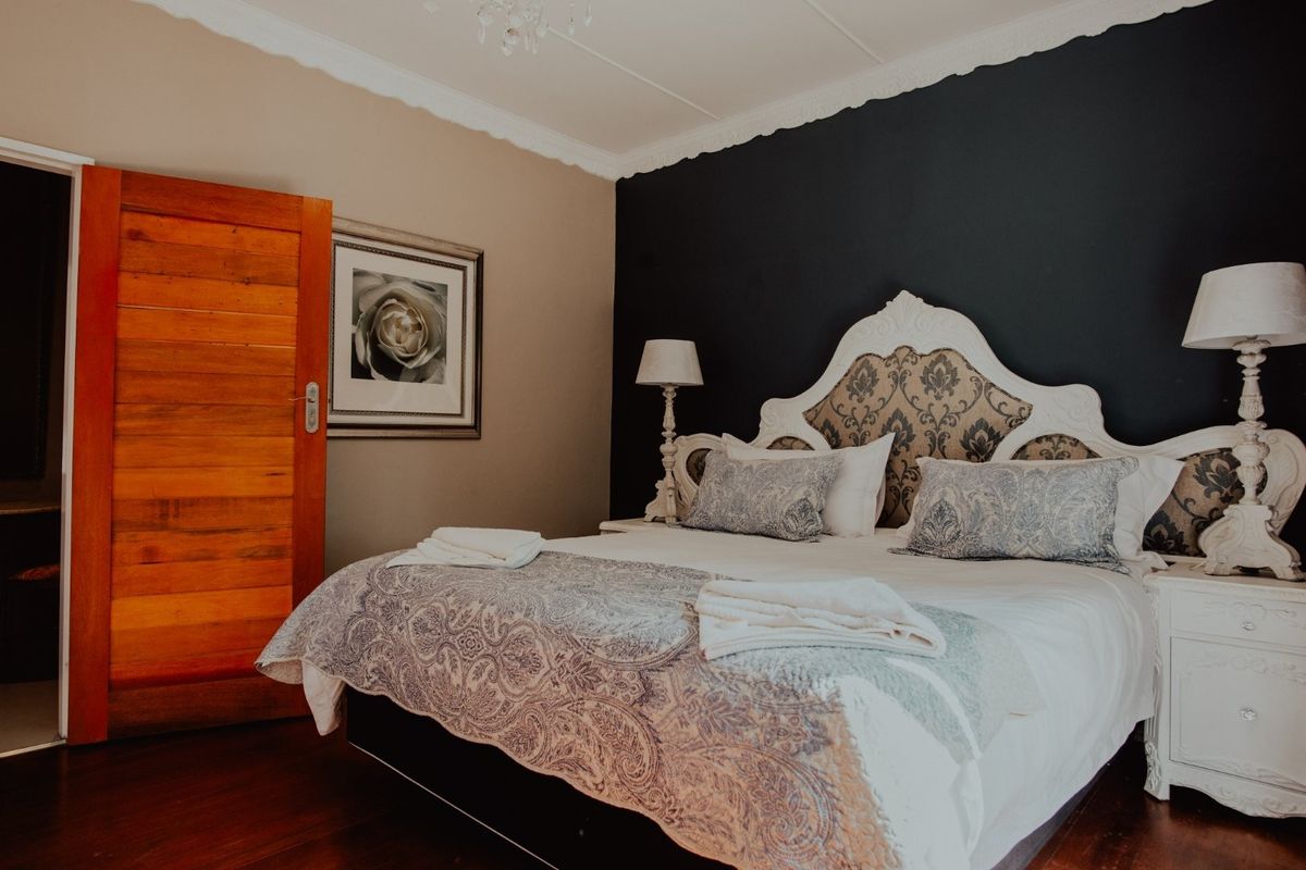 A well-appointed bedroom featuring dark accent wall, decorative crown molding, and warm wooden flooring.