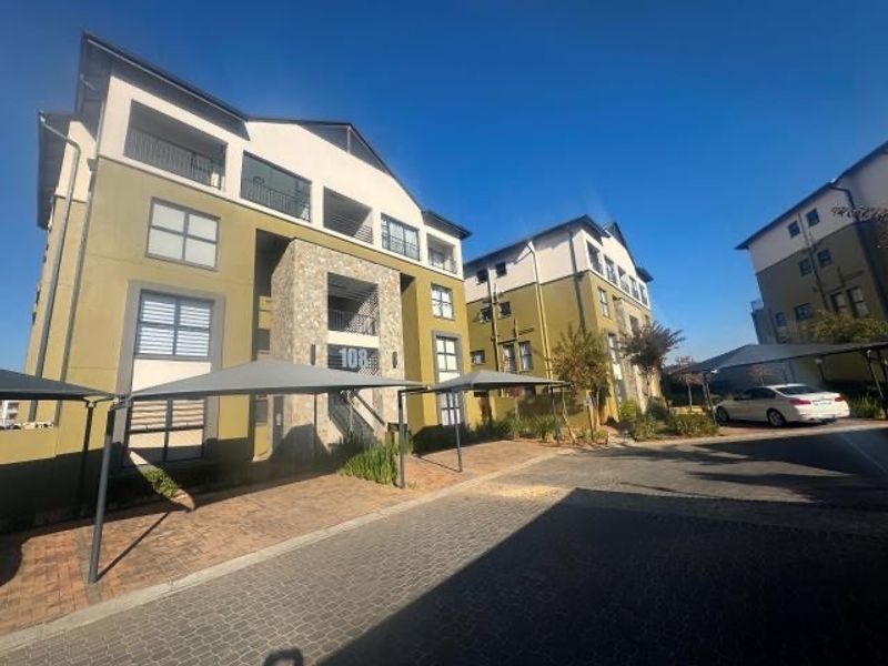 Exterior view of a modern apartment complex featuring stone cladding accents, paved driveway, and covered parking bays.