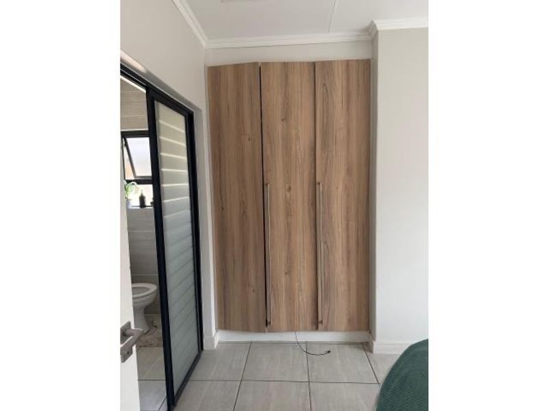 A bedroom featuring built-in wooden cabinetry and tiled flooring, with an adjacent bathroom visible through a modern black-framed glass door.