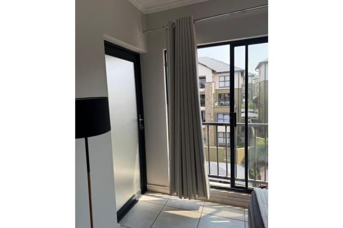 A bright bedroom area featuring tiled flooring, a sliding glass door leading to a balcony, and a frosted glass door.