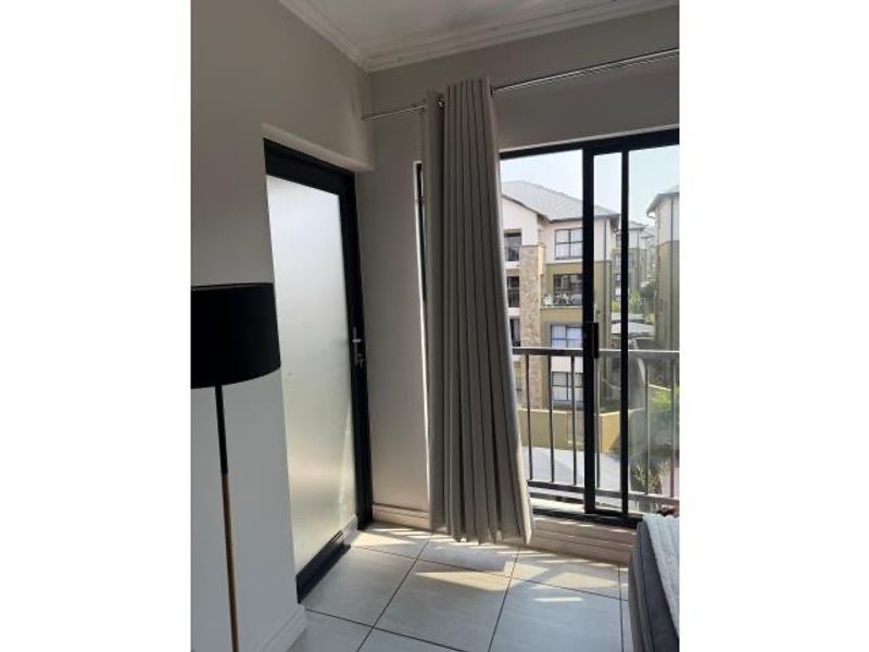 A bright bedroom area featuring tiled flooring, a sliding glass door leading to a balcony, and a frosted glass door.