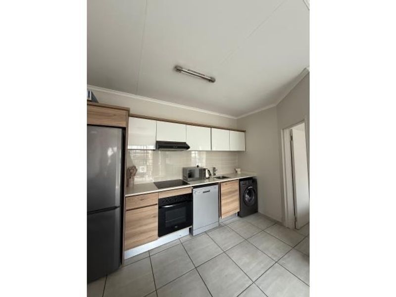 Modern kitchen featuring wood-grain cabinetry, integrated oven, hob, extractor fan, and tiled flooring with a dedicated space for laundry appliances.