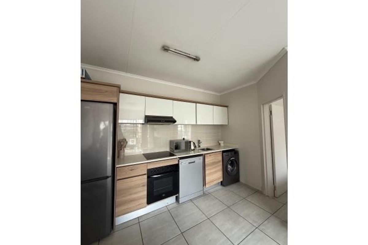 Modern kitchen featuring wood-grain cabinetry, integrated oven, hob, extractor fan, and tiled flooring with a dedicated space for laundry appliances.