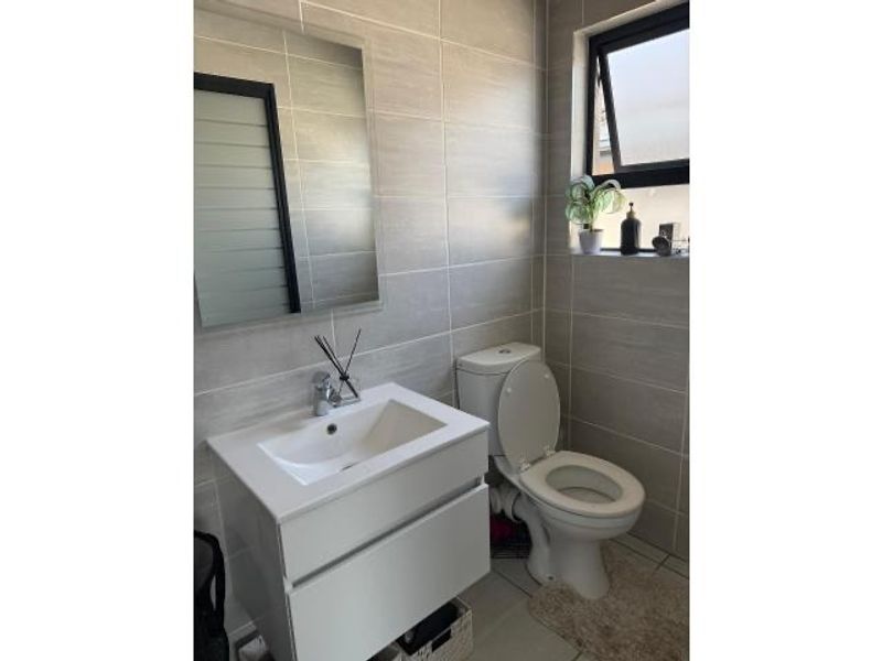 A modern bathroom featuring floor-to-ceiling wall tiles, a contemporary wall-mounted vanity with integrated basin, and a standard toilet.