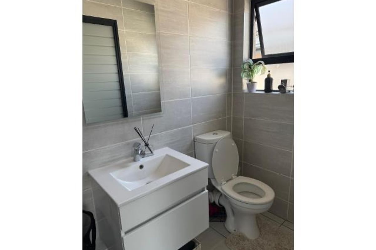A modern bathroom featuring floor-to-ceiling wall tiles, a contemporary wall-mounted vanity with integrated basin, and a standard toilet.